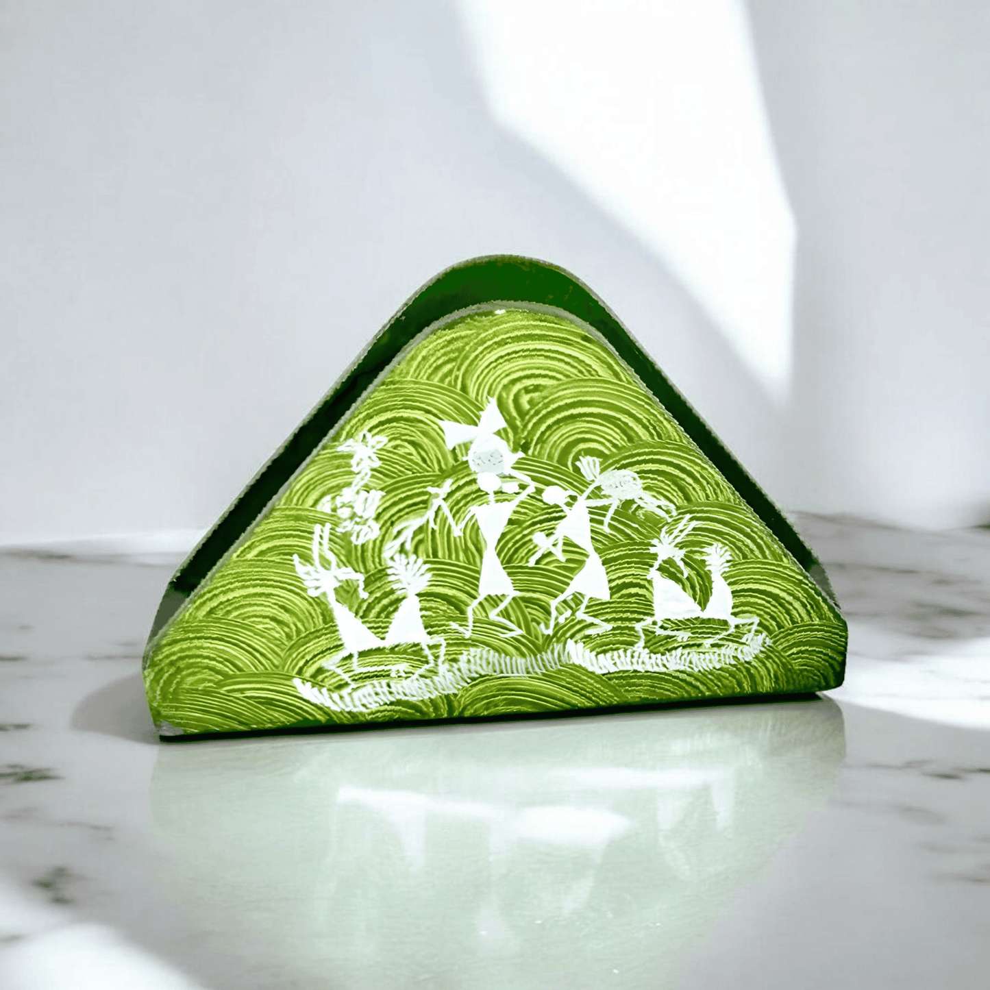 A triangular wooden napkin holder with Warli tribal artwork, predominantly green with white patterns