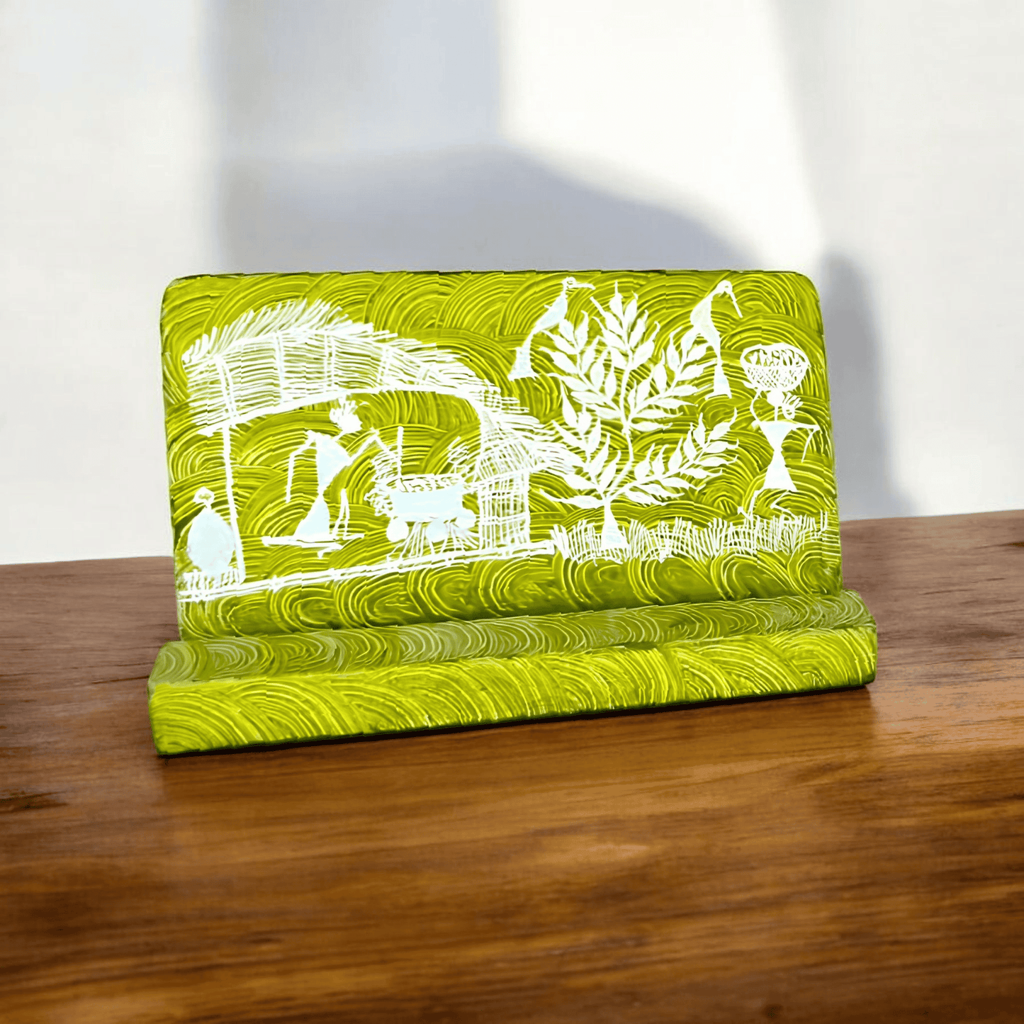 A green wooden mobile stand with hand-painted Warli tribal designs placed on a wooden surface.