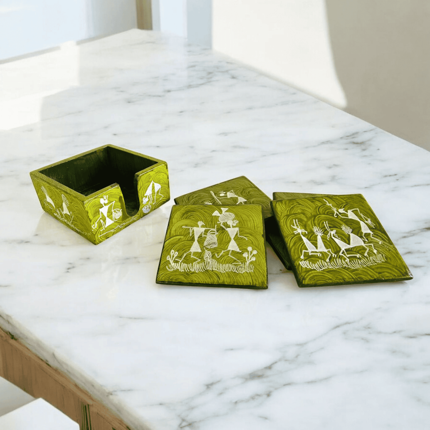 A set of handcrafted wooden tea coasters with Warli art designs, displayed on a marble surface, along with a matching holder.