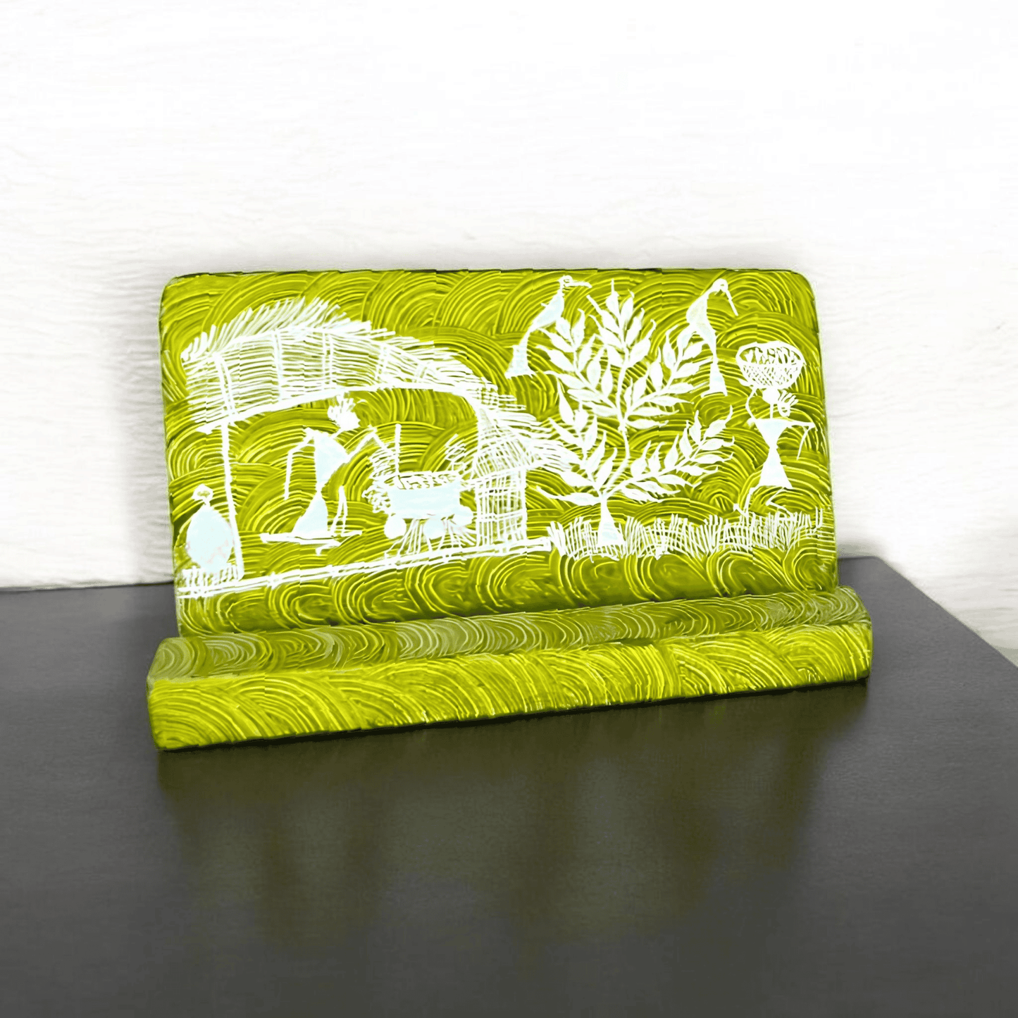 A green wooden mobile stand with hand-painted Warli tribal designs placed on a wooden surface.